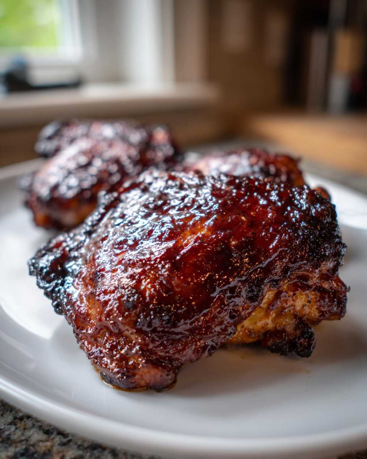A close-up of perfectly cooked Sticky BBQ Chicken Thighs with a dark, glossy, caramelized glaze and crispy edges.