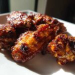 Close-up of several Sticky BBQ Chicken Wings Crispy Oven Style glistening with glaze on a white plate.
