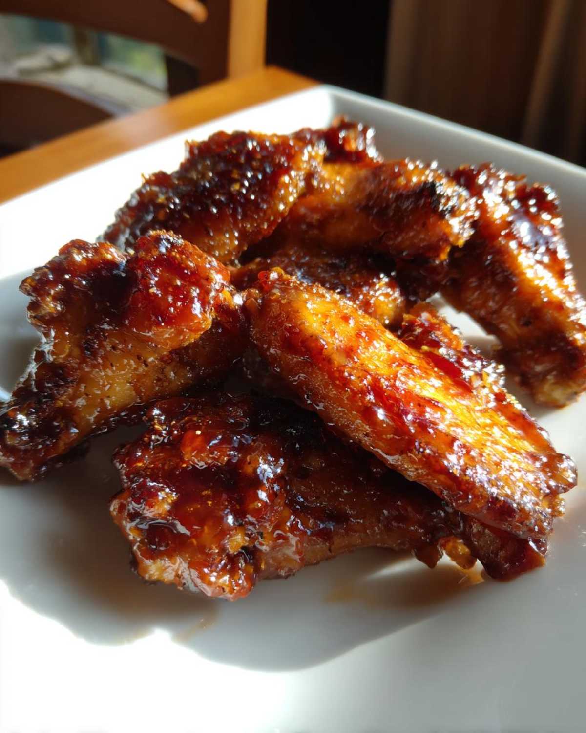 Close-up of several Sticky BBQ Chicken Wings Crispy Oven Style coated in a thick, glossy, dark brown glaze.