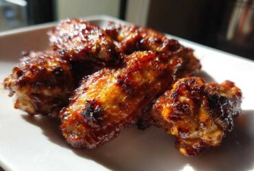Close-up of several Sticky BBQ Chicken Wings Crispy Oven Style glistening with glaze on a white plate.