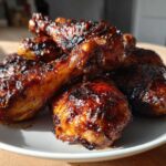 A pile of crispy Sticky Honey Garlic Chicken Drumsticks coated in a dark, glossy glaze on a white plate.