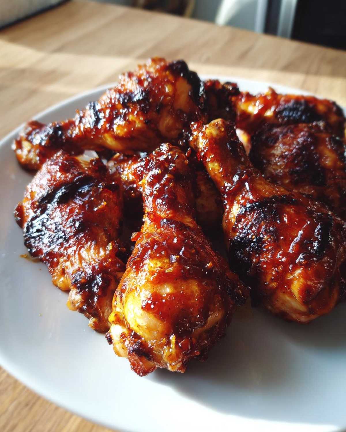 Close-up of several Sticky Honey Garlic Chicken Drumsticks Crispy with a dark, glossy glaze served on a white plate.