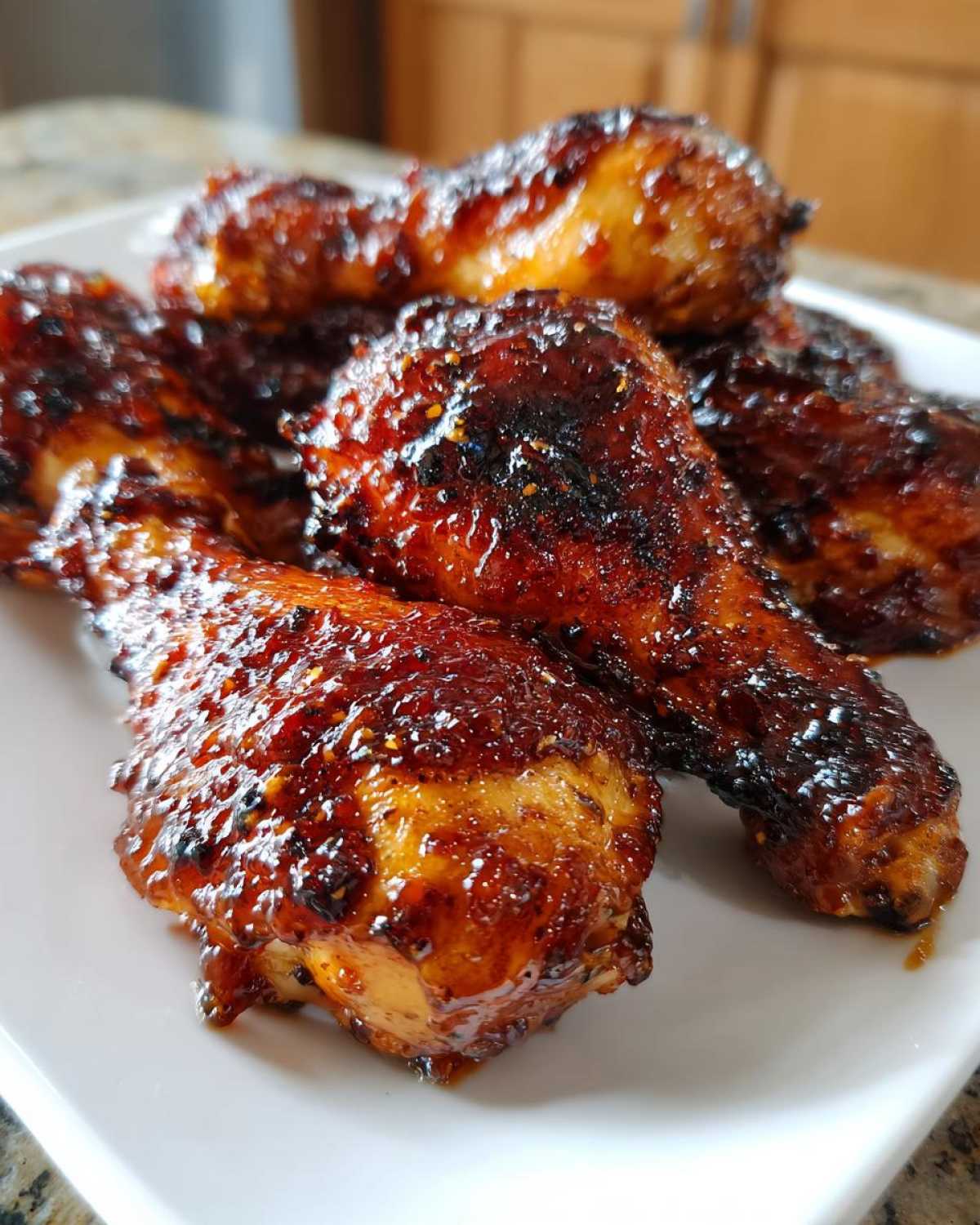 Close-up of several Sticky Honey Garlic Chicken Drumsticks Crispy, glazed with a dark, shiny sauce, served on a white plate.