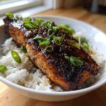 A perfectly cooked fillet of Sticky Honey Soy Salmon served over white rice and garnished with sliced green onions.