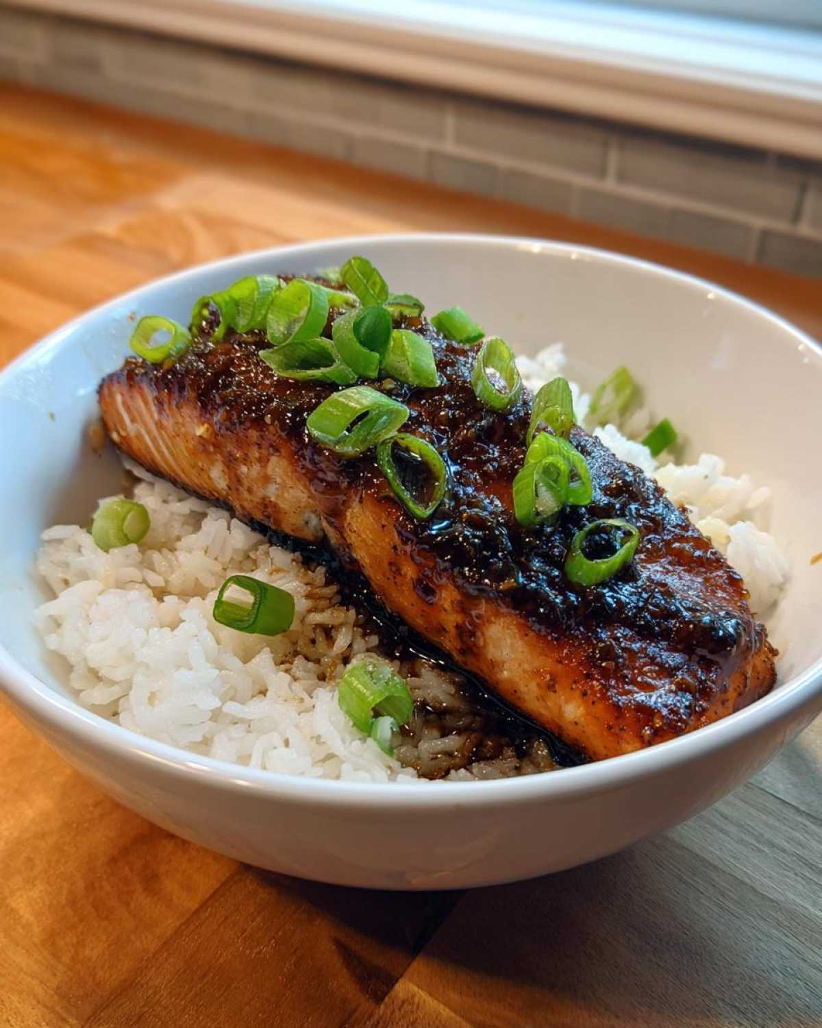 A close-up of a Sticky Honey Soy Salmon with Rice Bowl, featuring glazed salmon over white rice topped with sliced green onions.