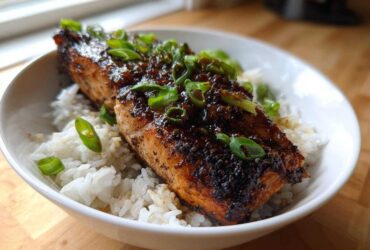 A perfectly cooked fillet of Sticky Honey Soy Salmon served over white rice and garnished with sliced green onions.