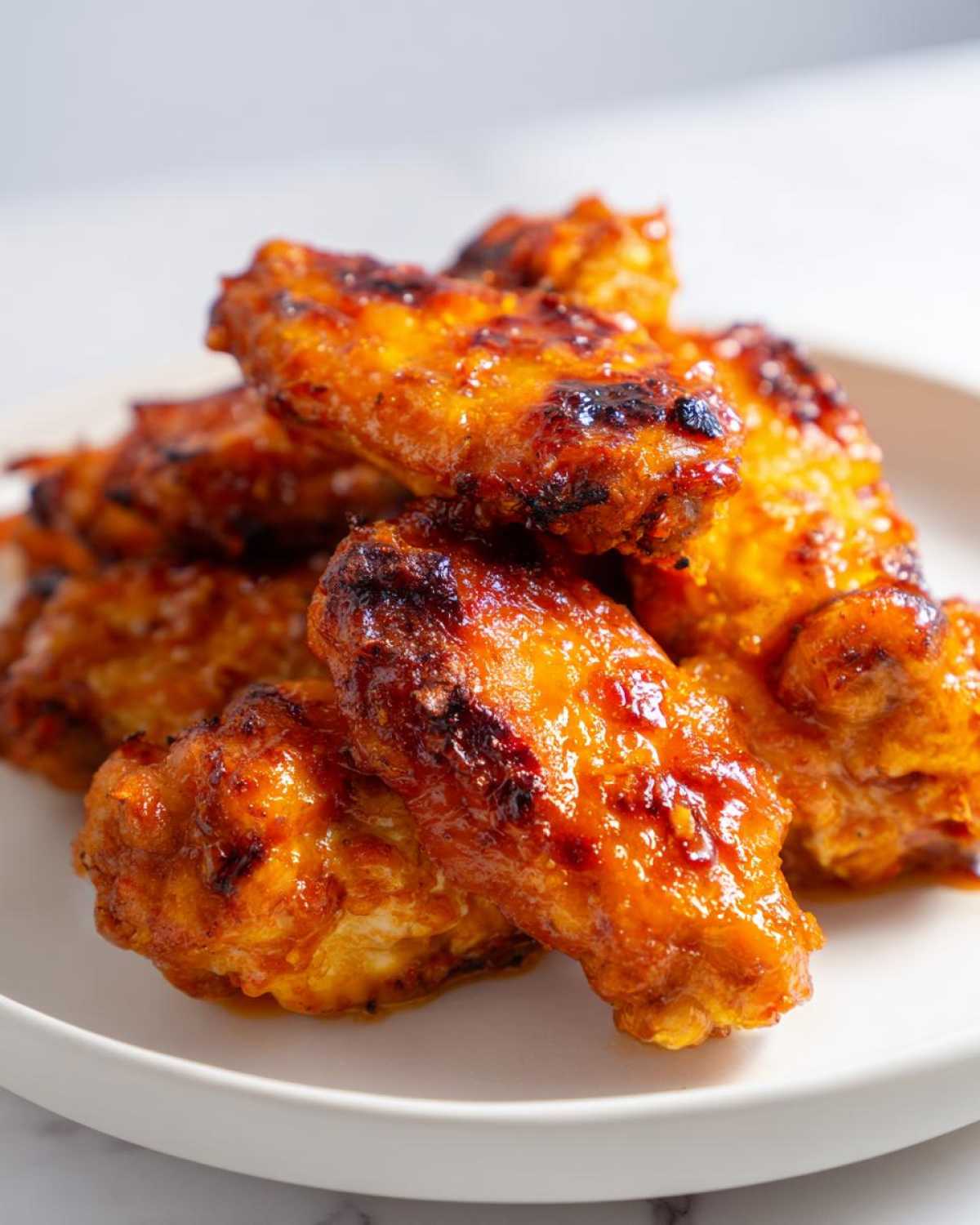 A close-up of several glossy, caramelized Sticky Orange Chicken Wings Crispy Oven Style piled on a white plate.