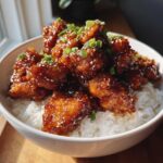 Close-up of a white bowl filled with white rice topped generously with glazed Sticky Sweet Chili Chicken.
