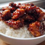 Close-up of a white bowl filled with white rice topped generously with pieces of Sticky Sweet Chili Chicken Bowl.