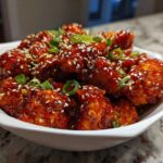 Close-up of Sticky Sweet Chili Chicken Easy Recipe pieces coated in glossy sauce, topped with sesame seeds and green onions.