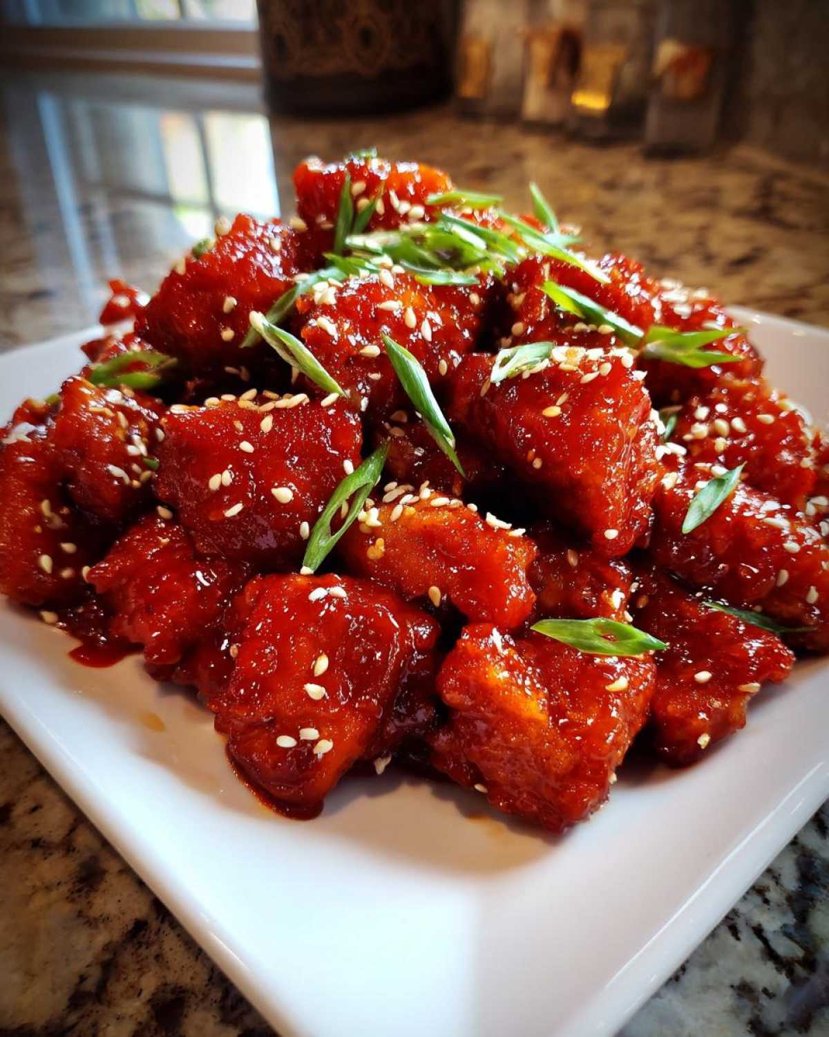 A mound of glistening Sticky Sweet Chili Chicken Easy Recipe pieces topped with sesame seeds and green onions.