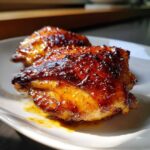 Close-up of two glossy, caramelized Sticky Sweet Chili Chicken Thighs Oven Baked pieces on a white plate.