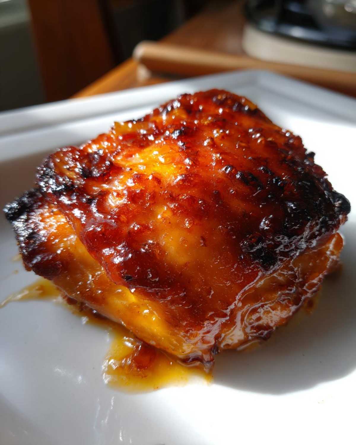 A close-up of a single, glistening Sticky Sweet Chili Chicken Thighs Oven Baked piece with a caramelized, dark orange glaze.