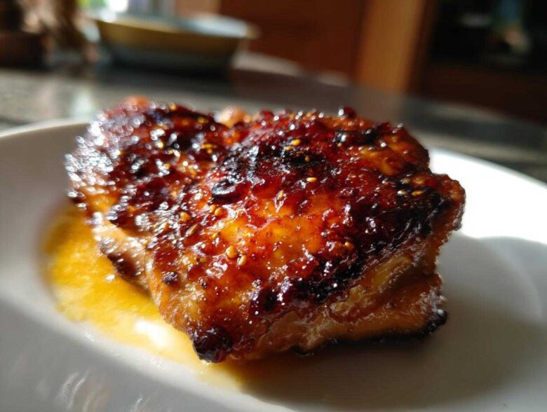 Close-up of a perfectly glazed Sticky Sweet Chili Chicken Thighs Oven Baked, glistening under light.