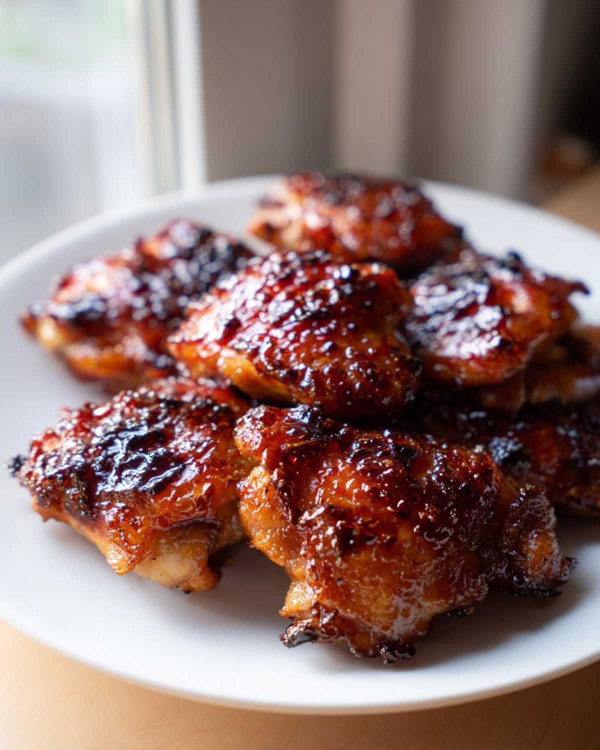 Close-up of several pieces of glazed Sticky Teriyaki Chicken Easy Weeknight Meal piled on a white plate.