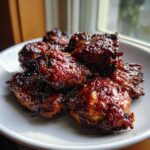 Close-up of several pieces of Sticky Teriyaki Chicken coated in a thick, dark, glossy glaze on a white plate.