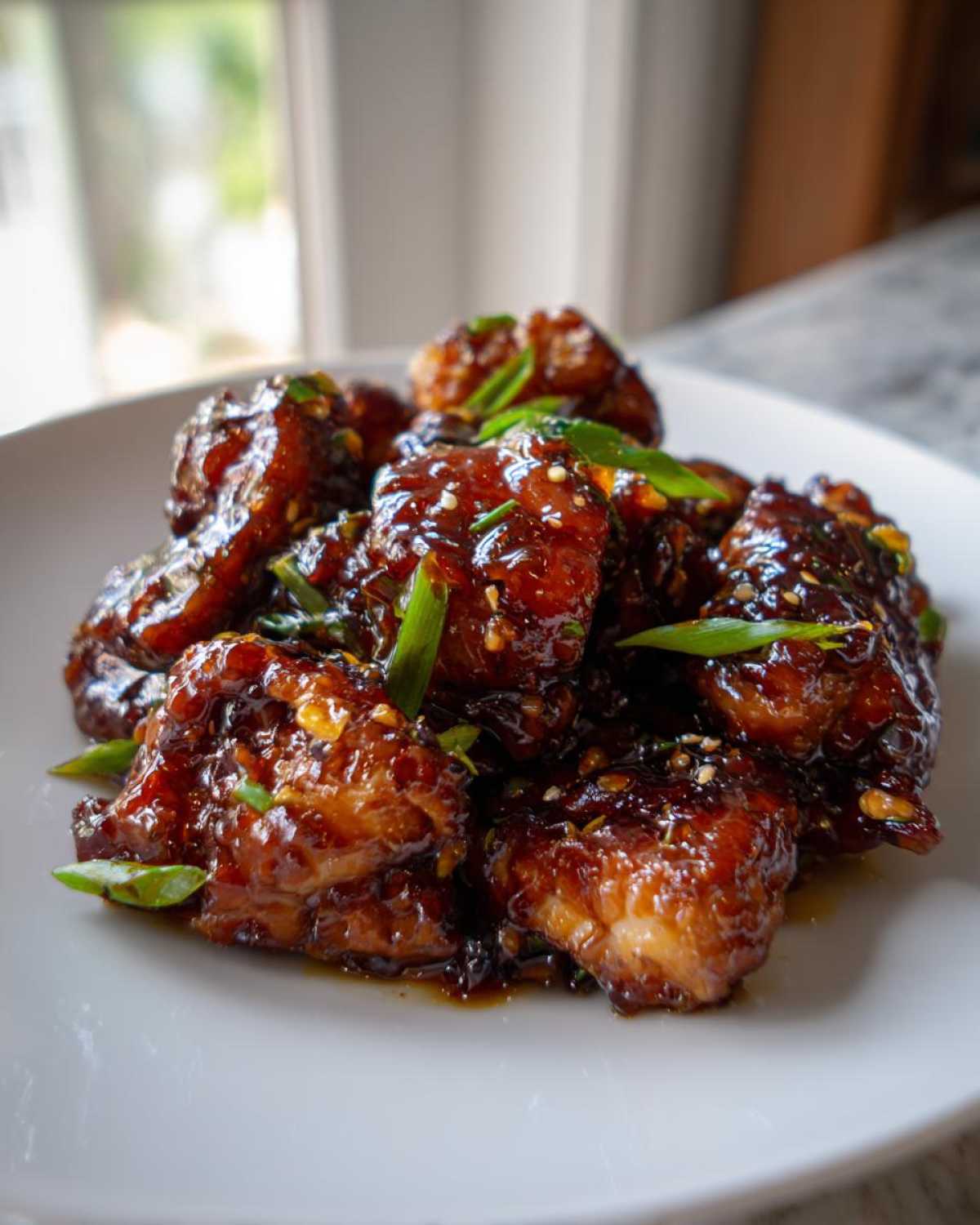 Close-up of glazed Sticky Teriyaki Chicken Thighs with Garlic, garnished with green onions and sesame seeds.