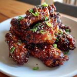 A close-up of several glazed Sticky Teriyaki Chicken Wings Oven Baked, topped with sesame seeds and green onions.