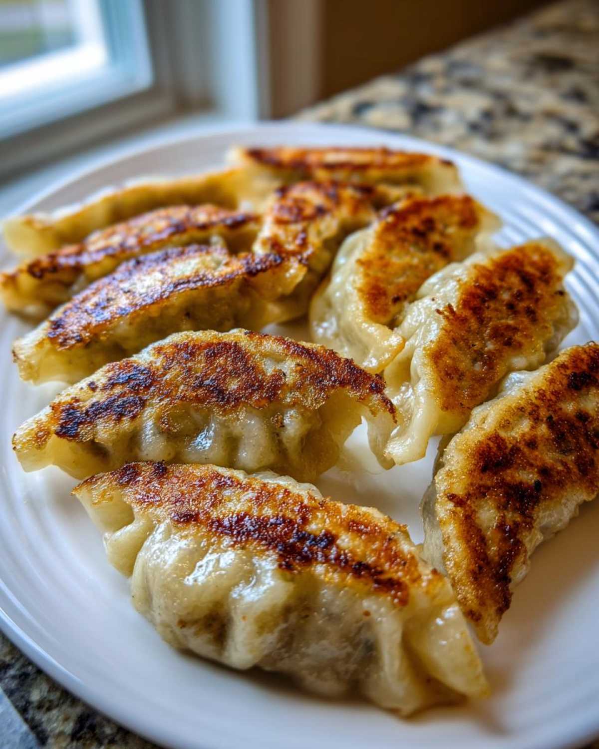 A plate piled high with golden-brown, pan-fried dumplings, showcasing their crispy bottoms.
