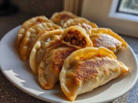 A plate of golden brown, pan-fried dumplings, with one dumpling cut open showing the savory filling.