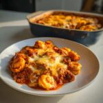 A serving of cheesy Beef Enchilada Tortellini on a white plate with the baking dish blurred in the background.