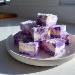 A stack of homemade Blueberry Fudge squares, featuring marbled purple and white layers, dusted with powdered sugar.