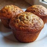 Three freshly baked Brown Sugar Banana Muffins with golden-brown tops resting on a white plate.