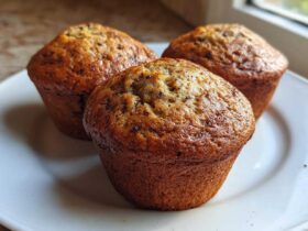 Three freshly baked Brown Sugar Banana Muffins with golden-brown tops resting on a white plate.