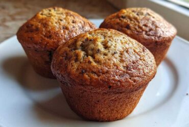 Three freshly baked Brown Sugar Banana Muffins with golden-brown tops resting on a white plate.