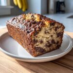 A golden-brown loaf of Chocolate Chip Banana Bread, sliced to show moist interior packed with chocolate chips.