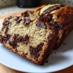 A close-up of two slices of moist Chocolate Chip Banana Bread showing swirls of melted chocolate chips.