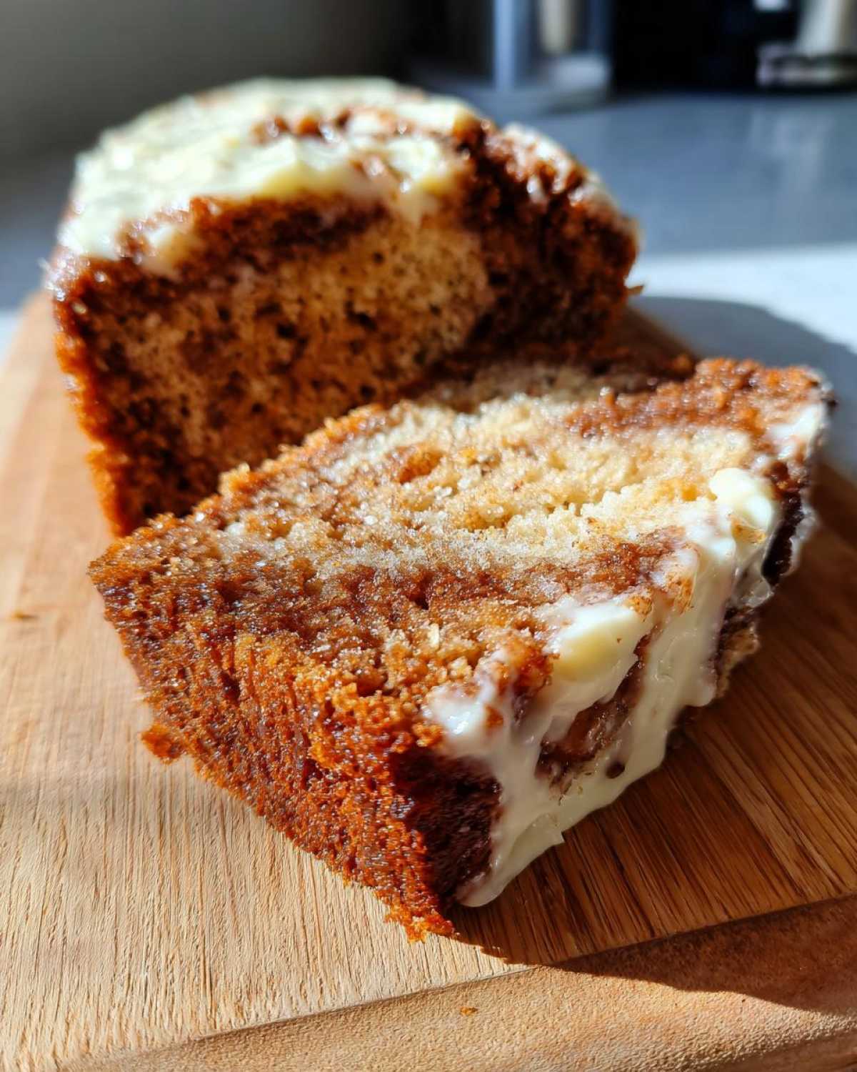 Close-up of a thick slice of Cinnamon Roll Banana Bread showing the swirl and generous cream cheese frosting.
