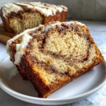 Close-up of a moist slice of Cinnamon Roll Banana Bread featuring a visible cinnamon swirl and cream cheese frosting.