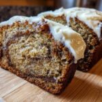 Two slices of Cinnamon Roll Banana Bread showing a swirl of cinnamon filling and topped with thick cream cheese frosting.