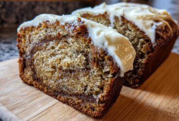 Two slices of Cinnamon Roll Banana Bread showing a swirl of cinnamon filling and topped with thick cream cheese frosting.