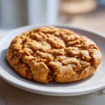 Close-up of a single, chewy Peanut Butter Cookies with classic crinkled top texture on a white plate.
