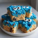 A stack of Cookie Monster Rice Krispy Treat Bars featuring blue frosting and candy eyes on a white plate.