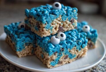 A stack of four bright blue Cookie Monster Rice Krispy Treat Bars topped with candy eyeballs on a white plate.