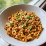A close-up of creamy, peanut-flavored Saucy Ramen Noodles topped with chopped peanuts and bright green scallions in a white bowl.