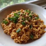 A close-up of creamy Saucy Ramen Noodles coated in a peanut sauce, topped with chopped green onions and crushed peanuts.