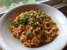 A close-up of creamy Saucy Ramen Noodles coated in a peanut sauce, topped with chopped green onions and crushed peanuts.