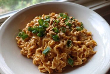 A close-up of creamy Saucy Ramen Noodles coated in a peanut sauce, topped with chopped green onions and crushed peanuts.