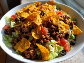 A vibrant bowl of Doritos Taco Salad featuring seasoned ground beef, lettuce, tomatoes, black olives, and crushed Doritos chips.