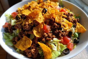 A vibrant bowl of Doritos Taco Salad featuring seasoned ground beef, lettuce, tomatoes, black olives, and crushed Doritos chips.