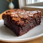 Close-up of a fudgy Brown Butter Brownies square topped with flaky sea salt on a white plate.