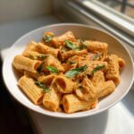 Close-up of rigatoni pasta coated in a rich tomato cream sauce, garnished with fresh basil, part of the Garlicky Pasta with Tomato Cream Sauce recipe.