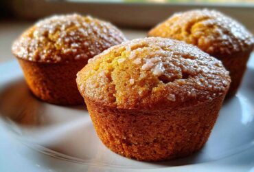 Three freshly baked Keto Lemon Muffins with a light lemon glaze topping resting on a white plate.