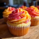 Close-up of a Mango Strawberry Sunset Cupcakes featuring bright yellow cake and vibrant pink and orange swirled frosting.