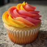 Close-up of a single Mango Strawberry Sunset Cupcakes featuring vibrant yellow, orange, and pink ombre frosting swirl.