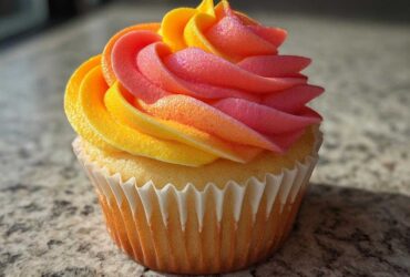 Close-up of a single Mango Strawberry Sunset Cupcakes featuring vibrant yellow, orange, and pink ombre frosting swirl.